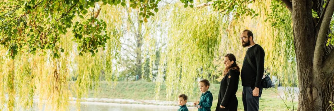 A family enjoys a peaceful walk by a lakeside under a willow tree during autumn.